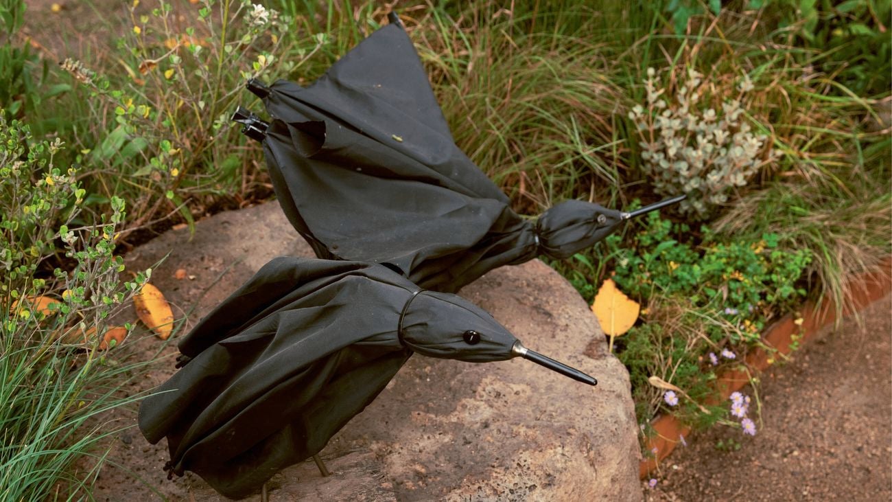 Two black umbrella bird shapes resting on a large rock in a garden bed.
