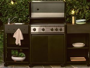 utdoor barbecue kitchen with BBQ, sink, and shelving against a green hedge with string lights