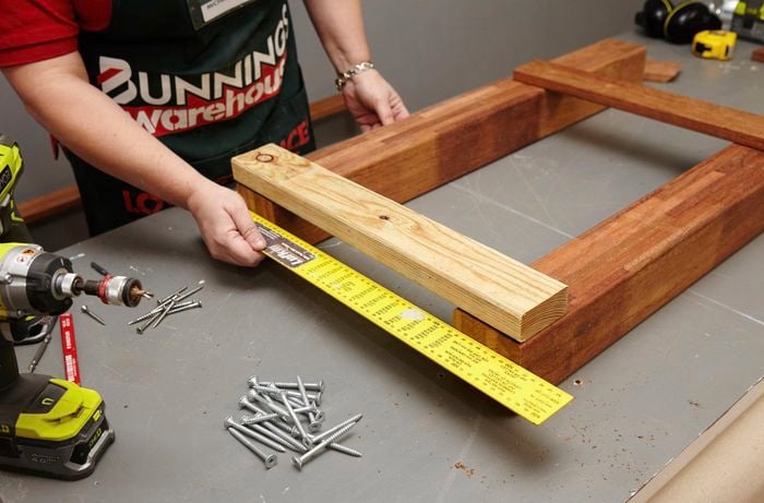 Person measuring wooden table legs with measuring tape.