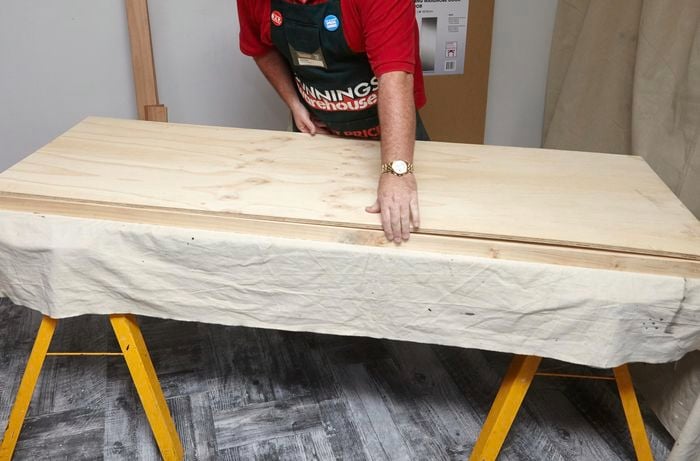 A person positioning a plywood sheet onto a timber frame