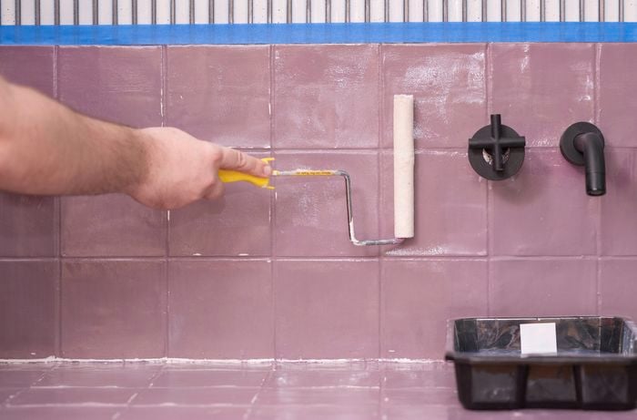 A person is using a paint roller to apply prime to tiles