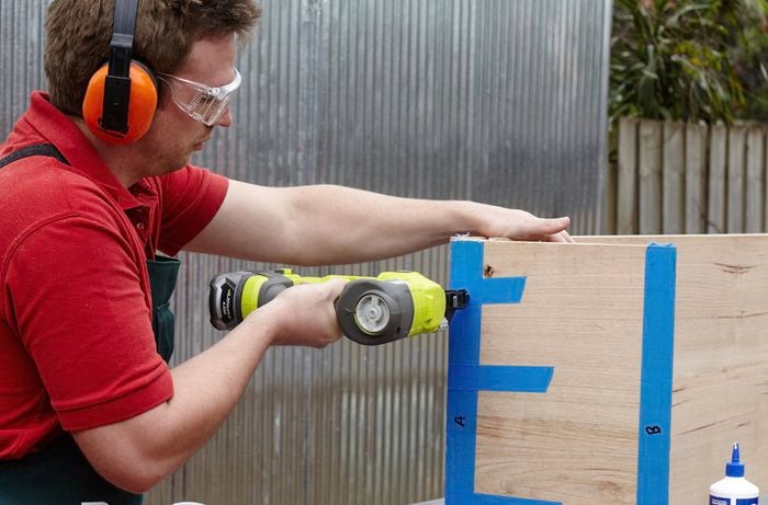 A person wearing protective gear joining two pieces of timber using a nail gun