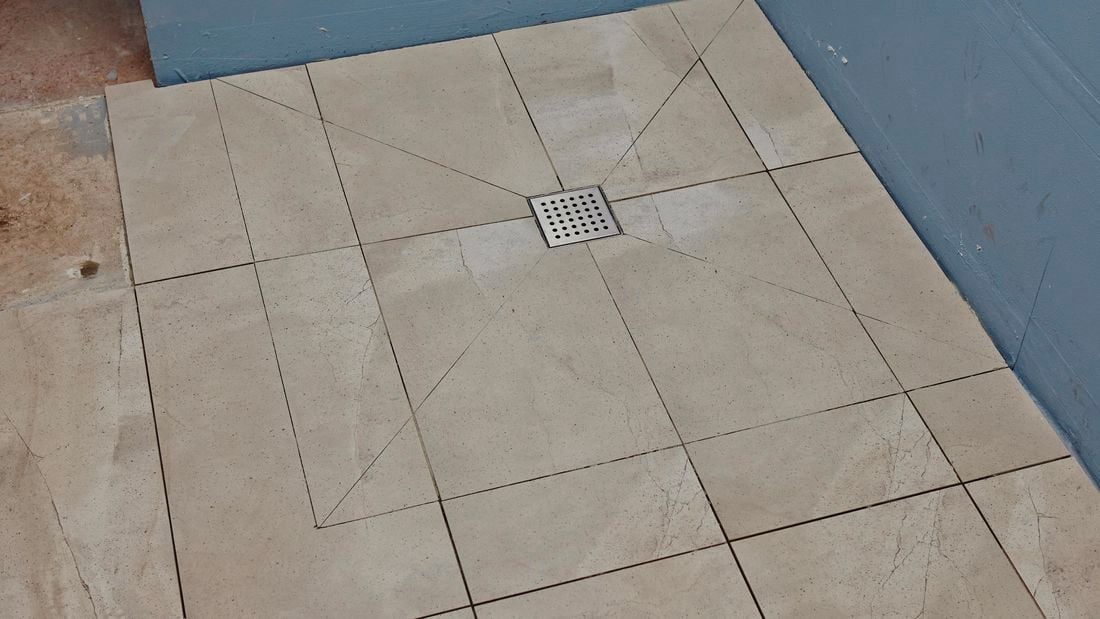 A tiled shower base with tiles cut on diagonals towards the drain hole