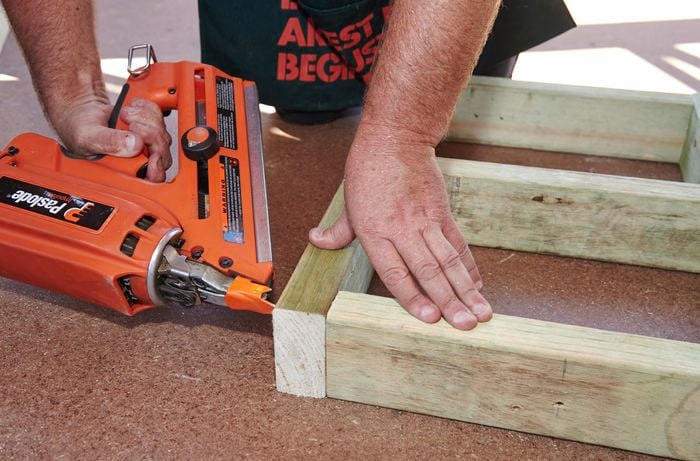 A person using a nail gun to join lengths of timber to make a frame