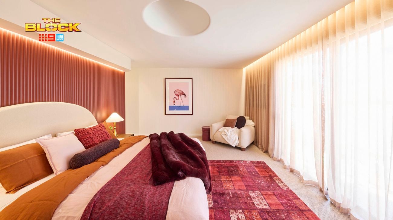 Bedroom with red rug, sheer curtains, and warm-toned bedding.