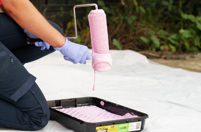 Person removing excess paint from a roller into a tray