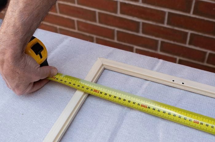  A person is measuring the new flyscreen mesh using a tape measure on a table for the installation .