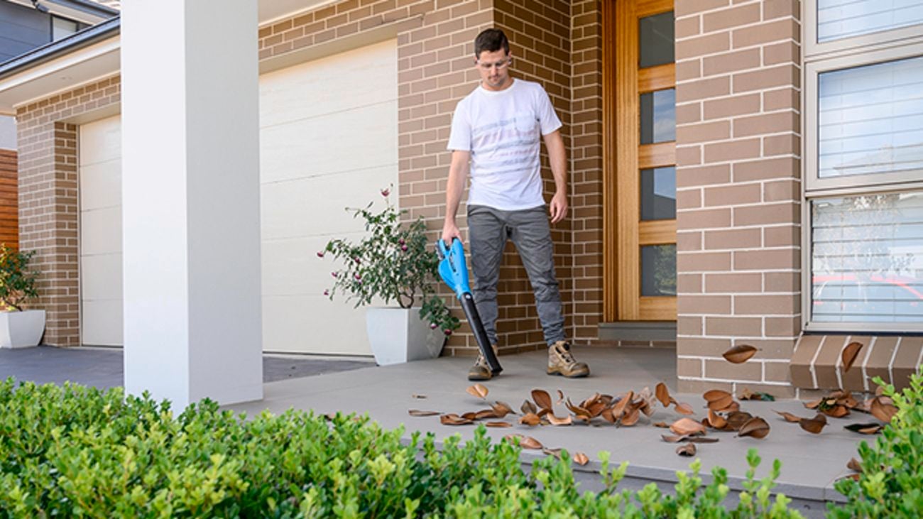 A man using a Victa leaf blower to blow leaves off the front porch.