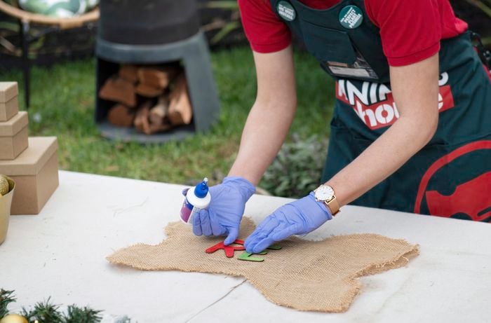 Person wearing gloves applying glue to fix letters to hessian