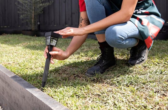 Person pushing a bollard solar garden light into grass beside a path