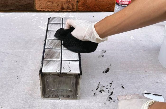 Using a black sponge to wipe black grout in the joints of a white tiled vase