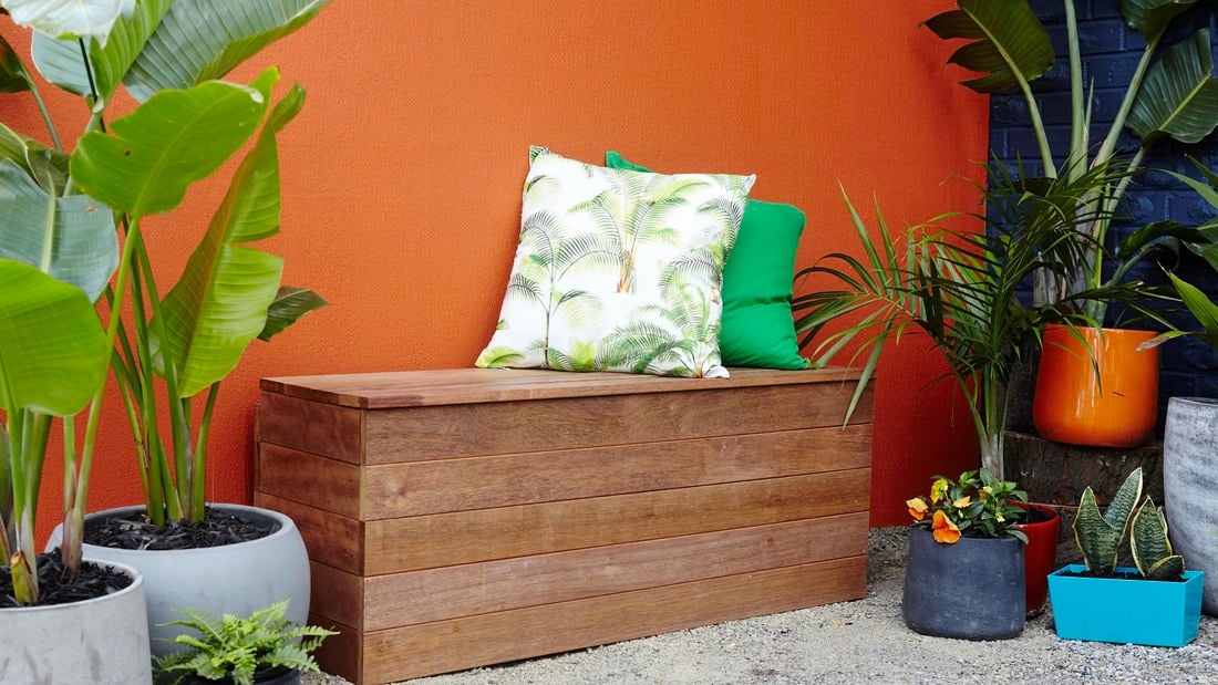 A finished bench seat with cushions and outdoor plants against an orange wall