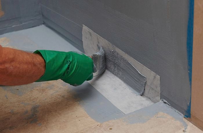 A person painting over a membrane sheet where the bathroom wall meets the floor