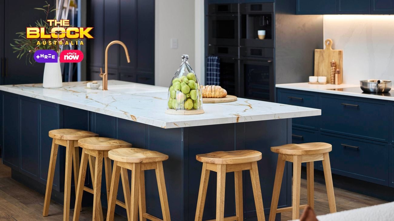 Kitchen island with marble top, gold faucet, and wooden stools.