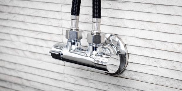 Close up image of a dual outlet garden tap connected to a white wall.