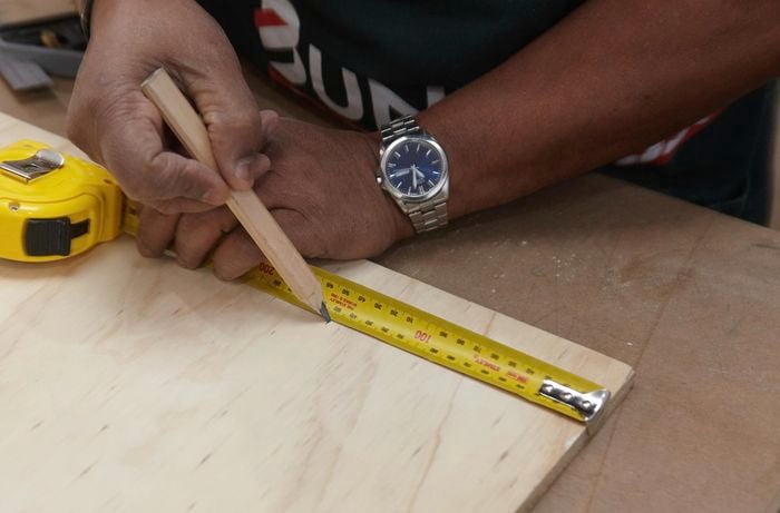Person measuring and marking ply panel with tape measure and pencil