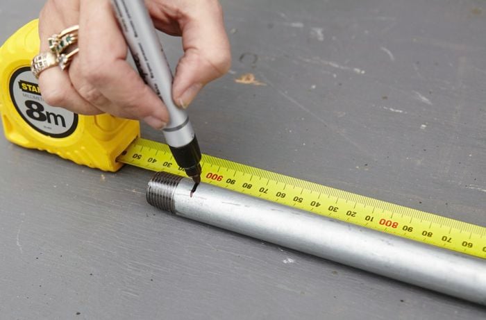 A person marking a measurement on a length of galvanised pipe