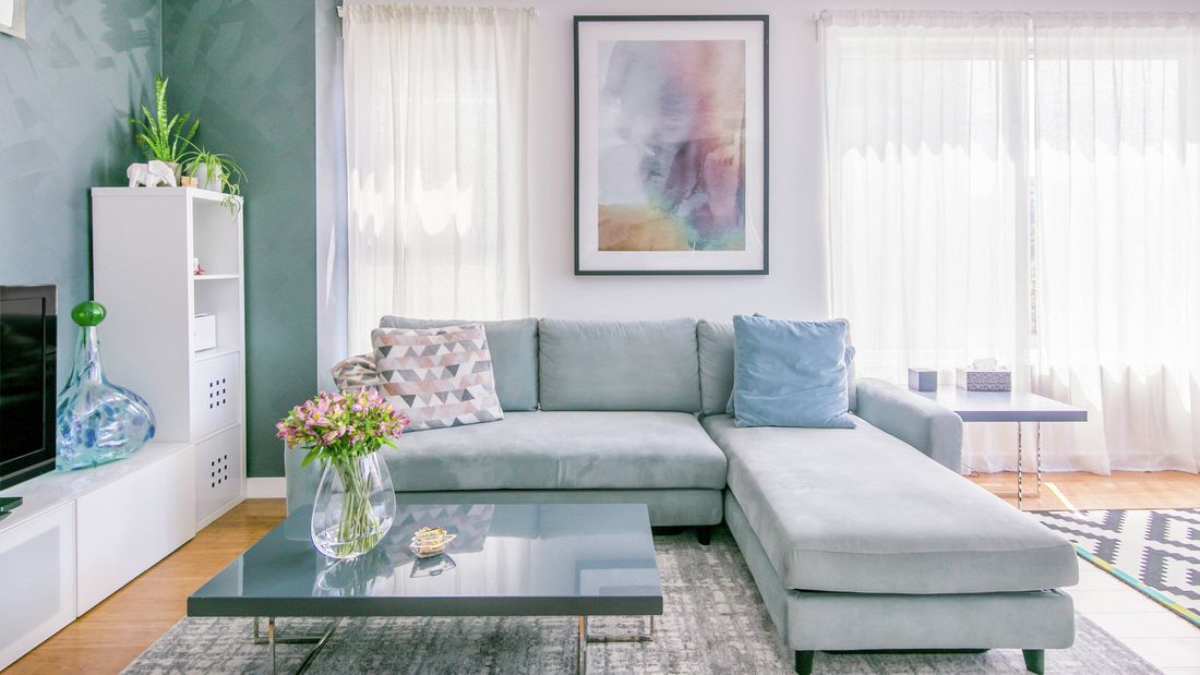 Living room featuring a light blue sectional sofa, dark grey coffee table with flowers, and large framed artwork on the wall.