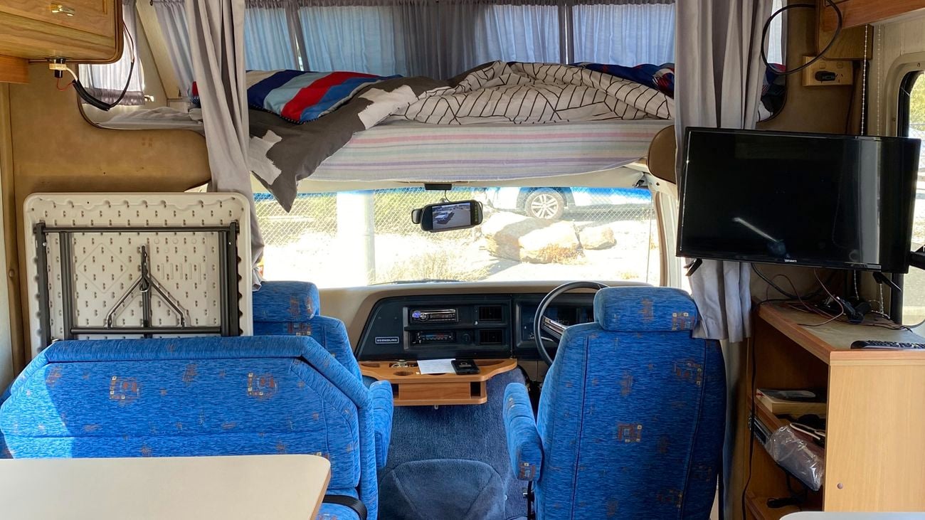 The interior of an old RV caravan with timber cabinetry and a blue couch.