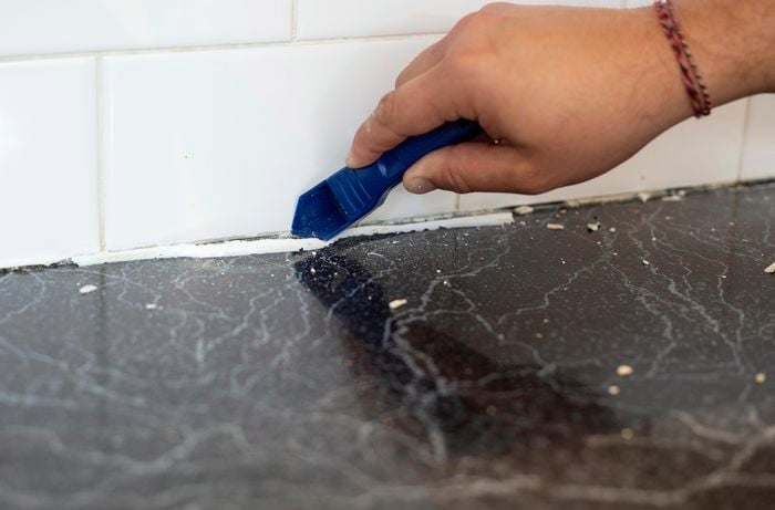 Person removing old grout between kitchen bench and wall tiles.