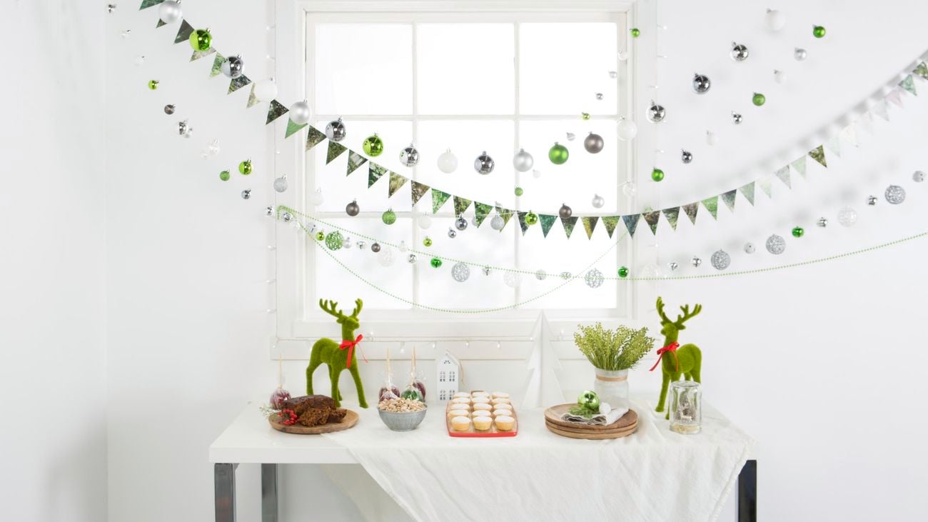 White table with Christmas party food and ornaments below decorative strings of baubles and bunting hung on wall hooks