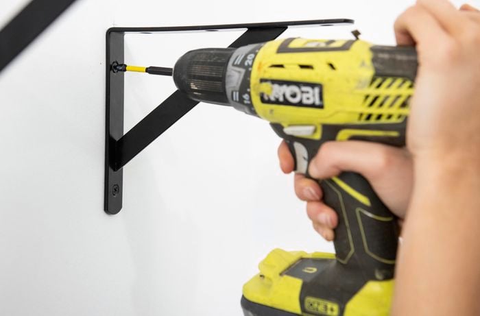 Person drilling black bracket into a wall.