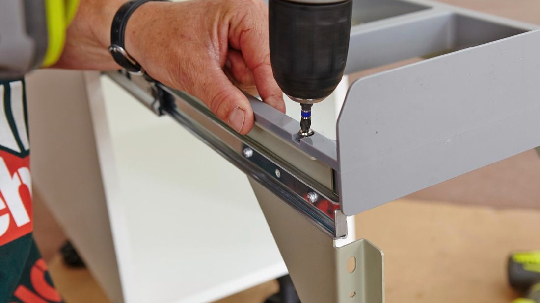 A person attaching a bin lid frame to drawer runners using a cordless drill 