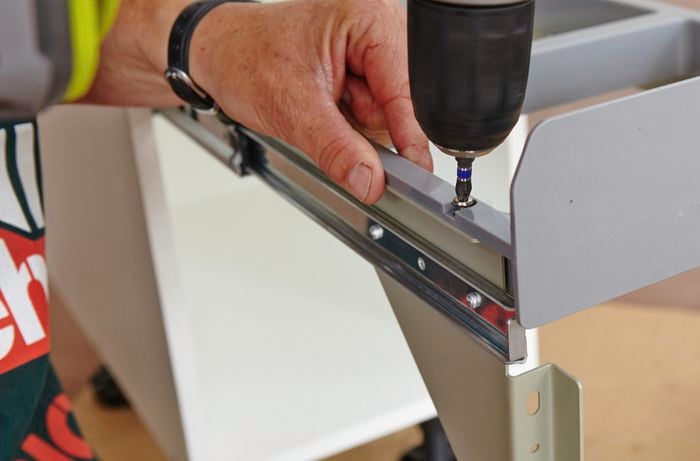 A person attaching a bin lid frame to drawer runners using a cordless drill 
