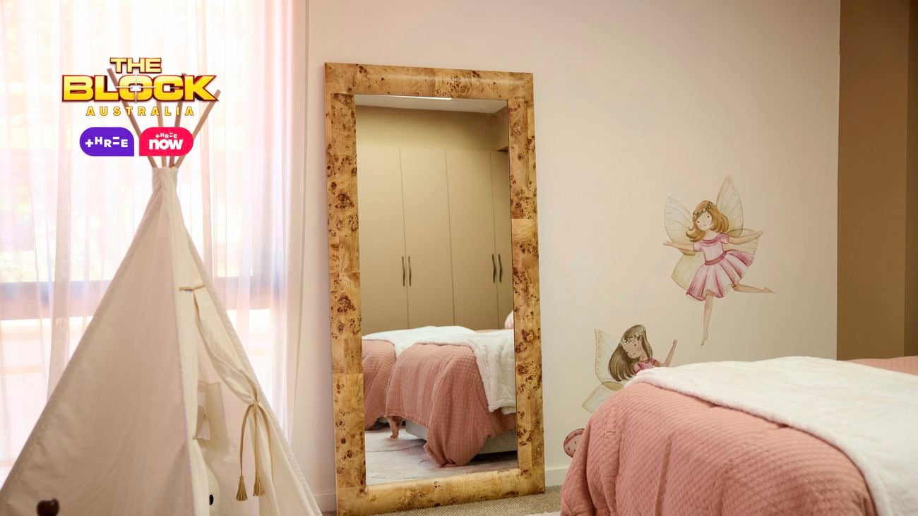 Cream bedroom with a mirror that is showing twin beds featuring blush linen. There is a teepee in the corner and fairy stickers on the wall.