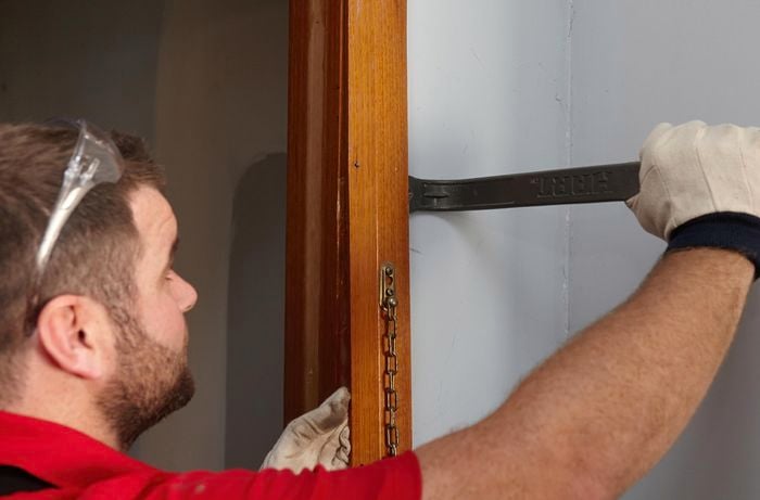 A door jamb being pried free from the wall with a pry bar