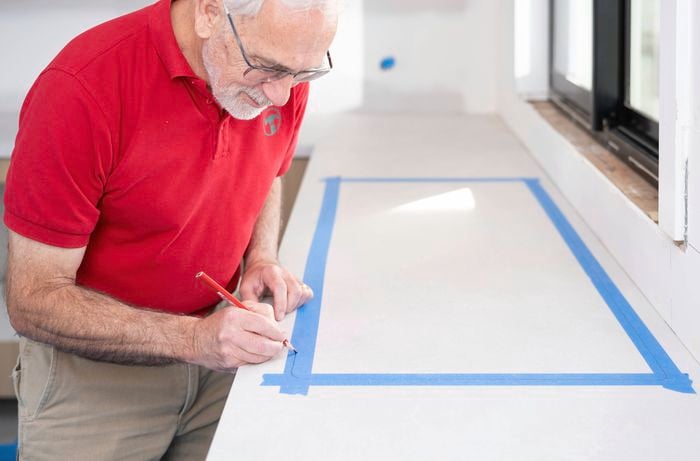 A Bunnings Team Member is marking the cut-out location on a laminate benchtop using a pencil and masking tape.