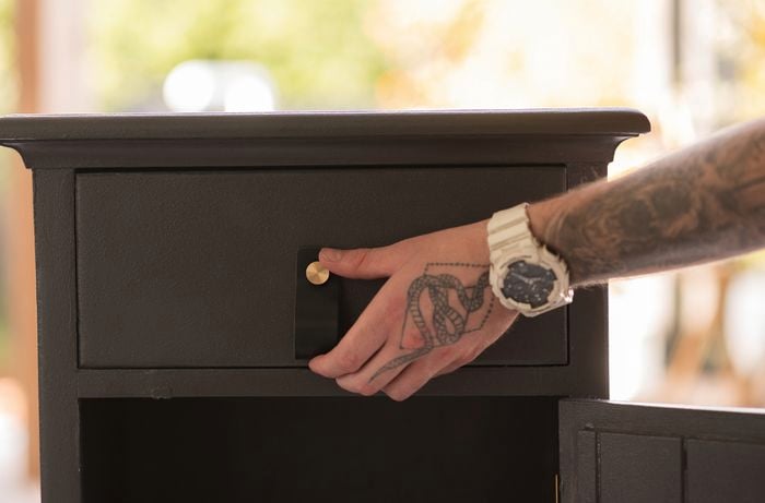 A hand on the black bedside table drawer handle.