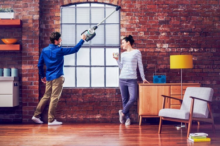 A man using a hand vacuum with an extended reach attachment to vacuum a brick window arch while a woman looks on