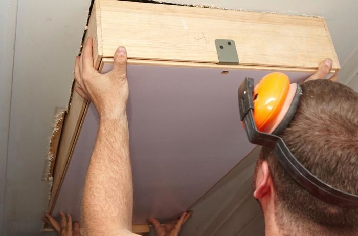 A person lifting an attic ladder into position in a hole in a ceiling