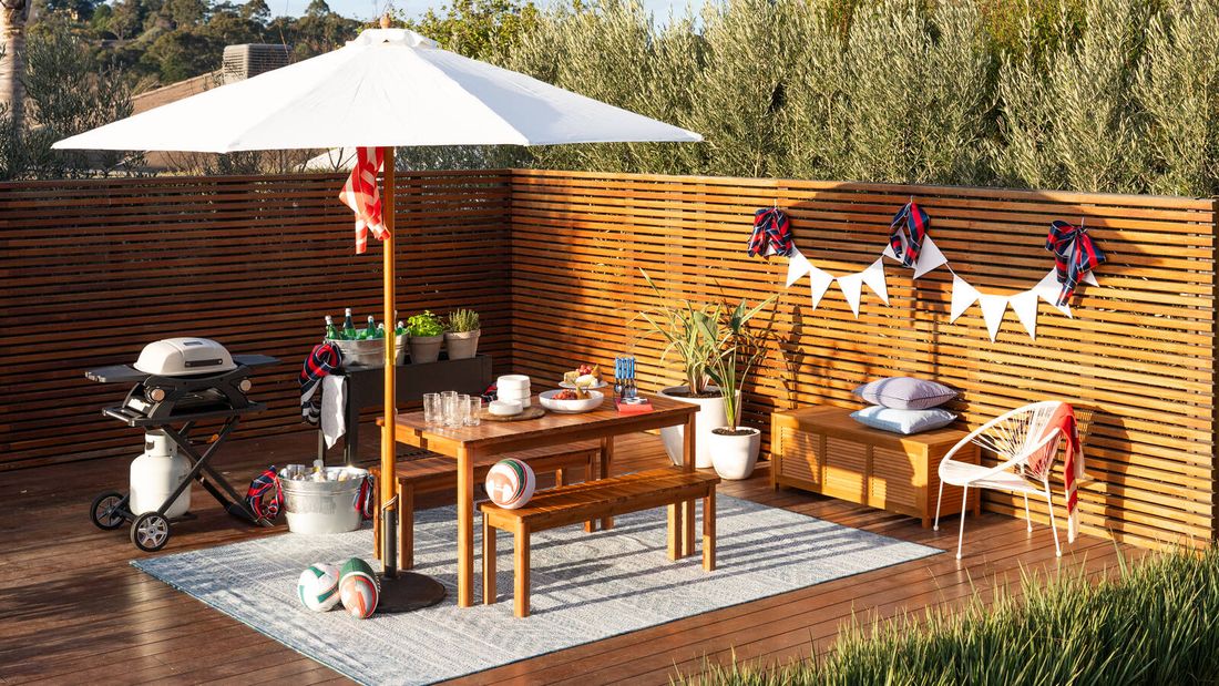 Decorated outdoor entertaining space with barbecue, dining table, bunting and sporting accessories.