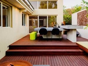 Decking with an outdoor table, outdoor bench and chairs on it at the back of a house.