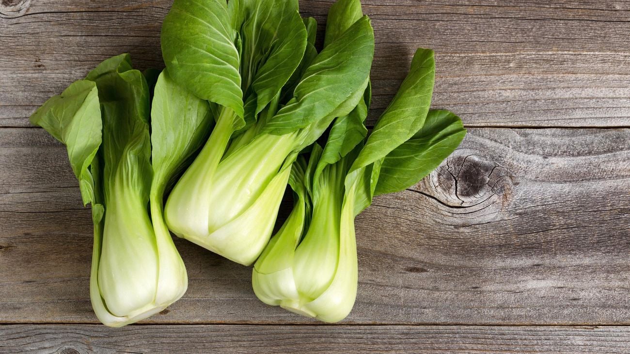 Overhead shot of three bunches of bok choy with large green leaves on a wooden background.