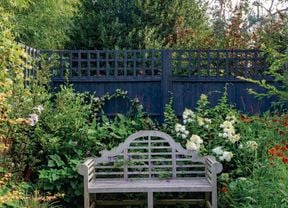 Pathway leads to outdoor bench seat surrounded by a variety of greenery and flowers.