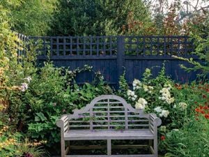 Pathway leads to outdoor bench seat surrounded by a variety of greenery and flowers.