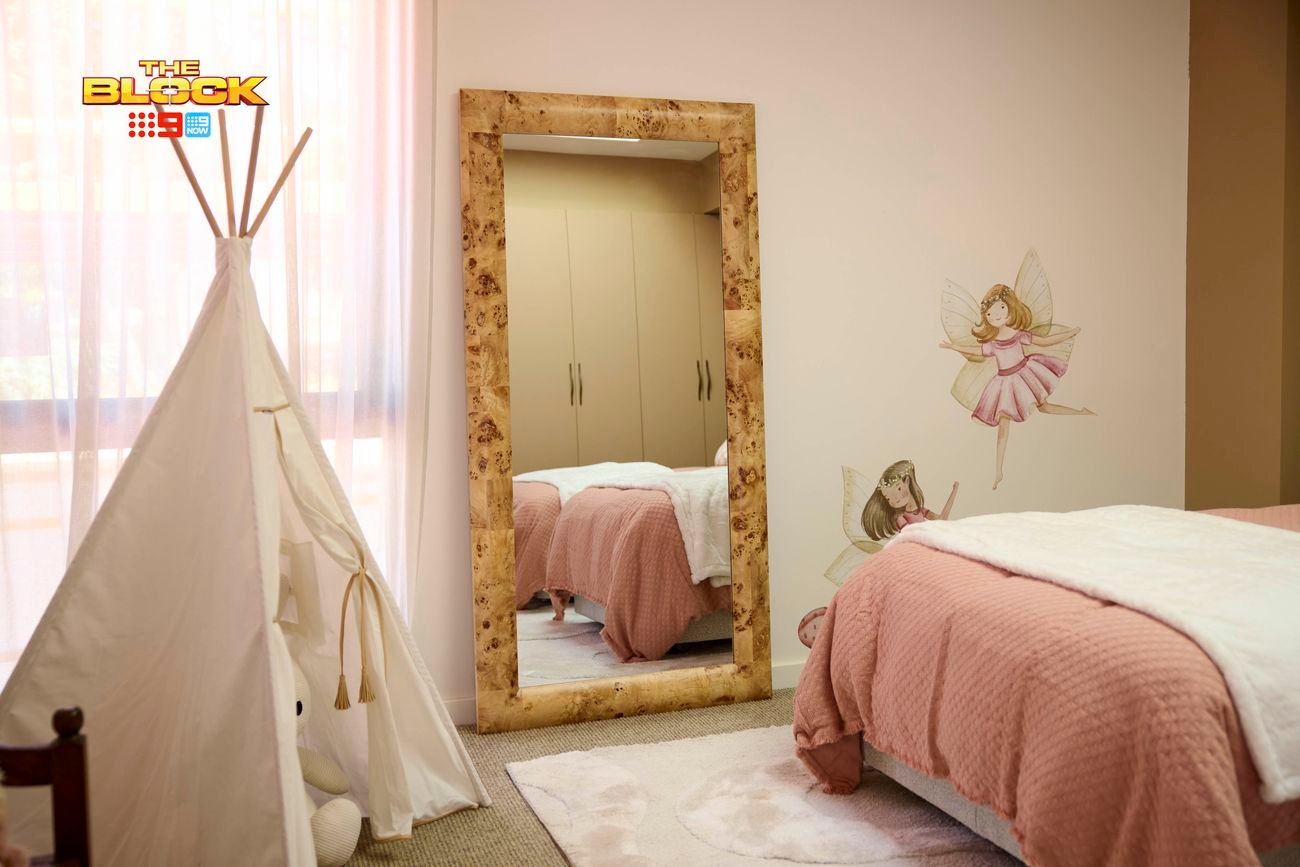 Cream bedroom with a mirror that is showing twin beds featuring blush linen. There is a teepee in the corner and fairy stickers on the wall.