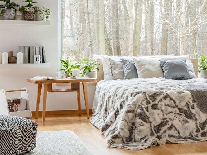 A bedroom with a bed, table and shelving on the wall in it