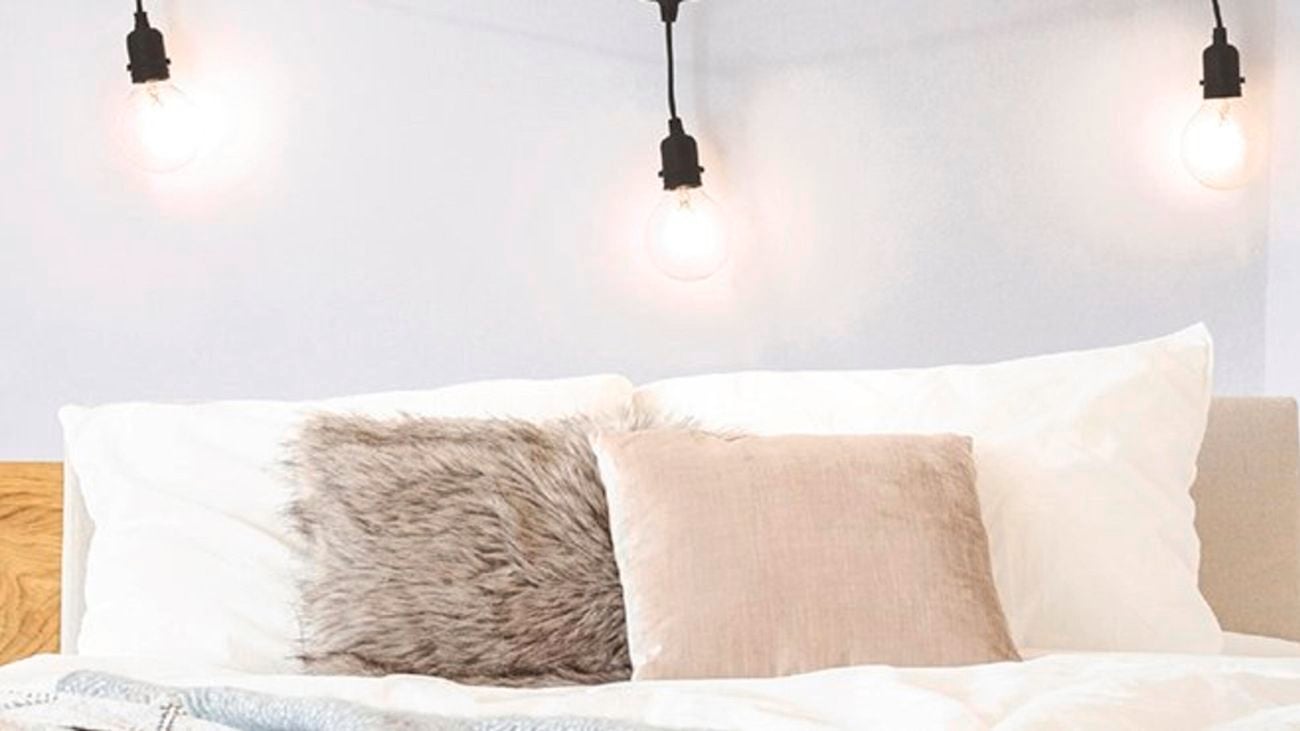 A bed with cushions on it and a string of light bulbs hanging above it.