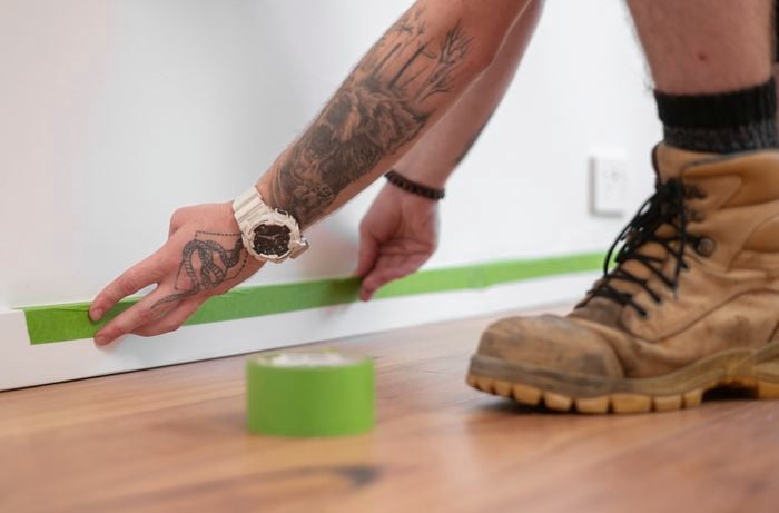 A person's hand is applying green colour painters tape on the edges.]