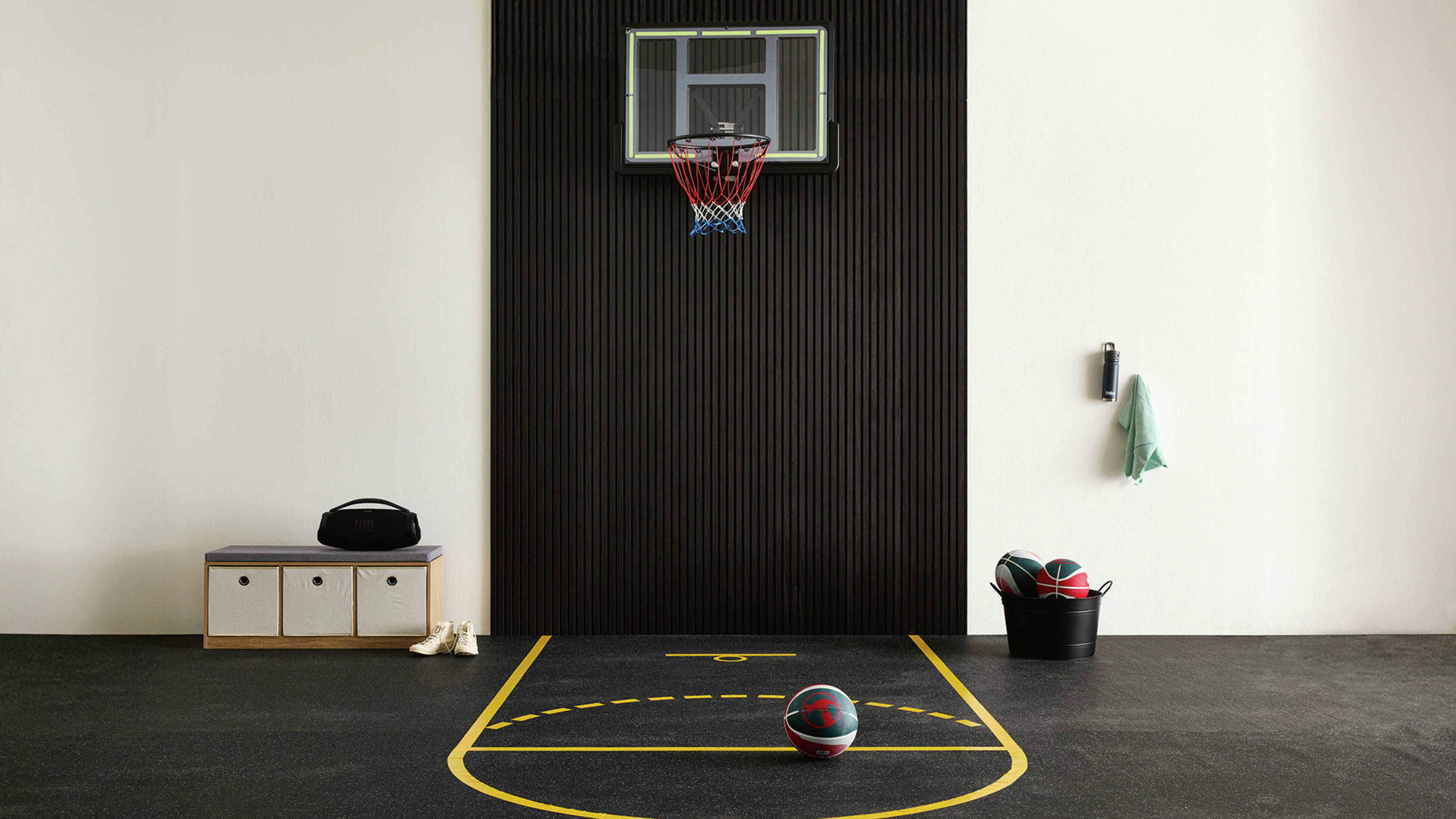 An indoor mini basketball court with a wall-mounted hoop on acoustic panelling and court lines marked on rubber matting with anti-slip tape