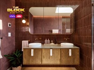 Modern bathroom with double round sinks on a wooden vanity, large mirror, maroon tiled walls, and partial view of a glass shower. 