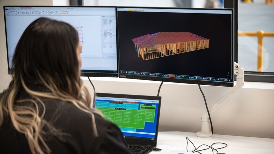 A lady sitting in a office working on three computer monitors