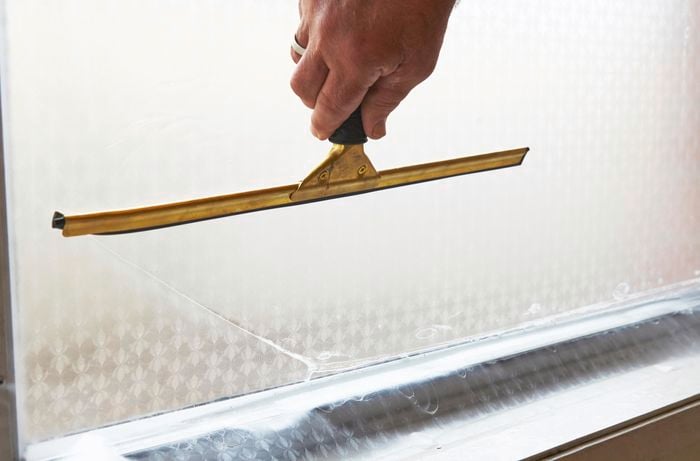 A person using a squeegee to push liquid and air bubbles from frosting on a window