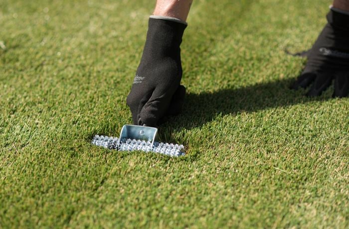 A person wearing gloves is using a synthetic turf join roller to roll over the joins to set the adhesive
