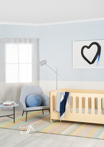 Detail of room painted pale blue and white with a blond wood baby's cot and striped pastel rug