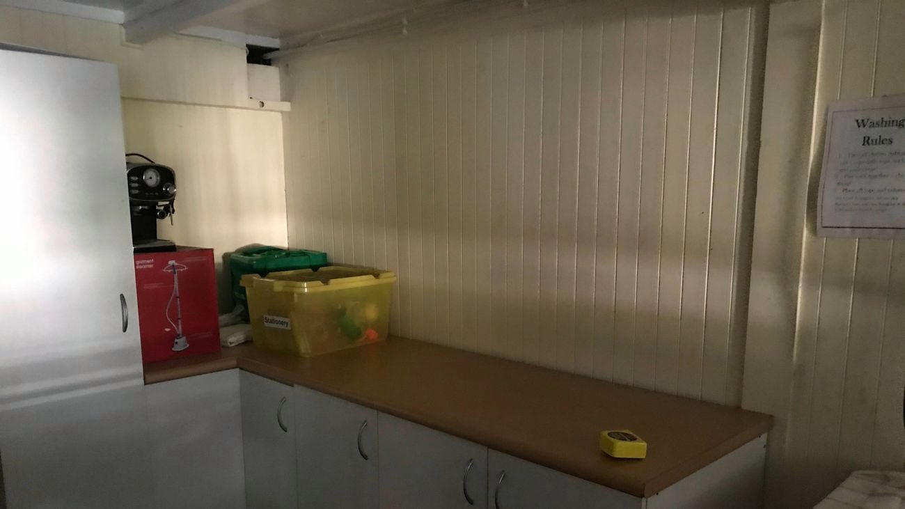 A room with white cupboards, painted timber walls and boxes on a timber benchtop.
